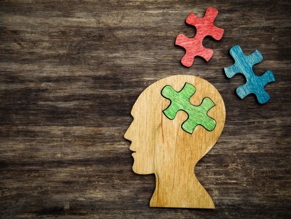 Human head silhouette with a jigsaw piece cut out on the wooden background, mental health symbol
