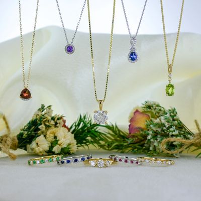 Elegant gemstone necklaces and rings displayed with flowers on a soft fabric.