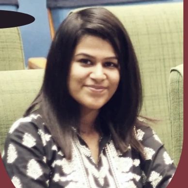 Young woman with straight black hair smiling at the camera indoors.