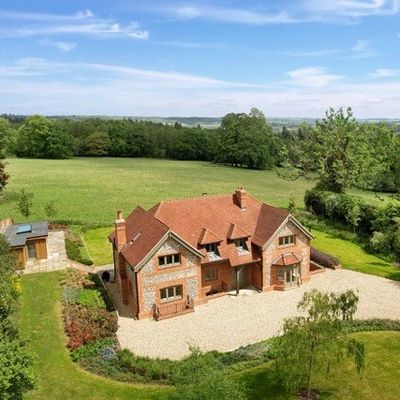 Large brick house with red roof in a spacious green countryside area.