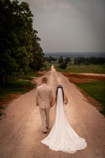 Bride and groom walking hand in hand down a dirt road.