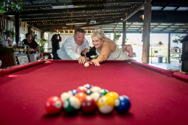 Newlyweds play pool together in a lively venue with joyful expressions.