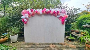 Pretty pink and white paper garland with honeycomb, fans and flowers on white washed plywood backdro