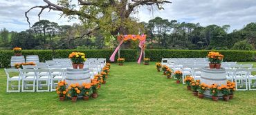 Bright pink and orange wooden wedding arch and seating with potted flowers at Indian wedding at The 