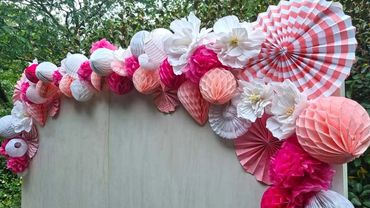 Pretty pink and white paper garland with honeycomb, fans and flowers on white washed plywood backdro