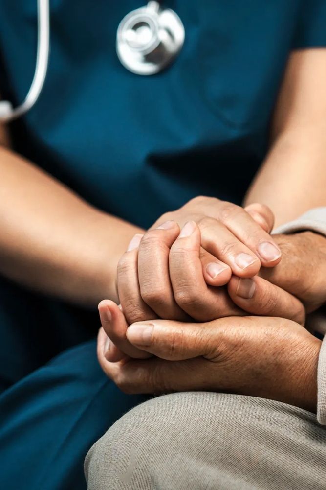 Medical professional holding a stethoscope, dressed in a white coat and blue scrubs.