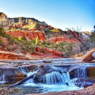 A small waterfall flows over red rocks in a desert canyon landscape in Sedona, AZ.