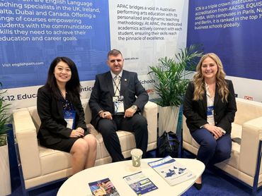 Three professionals seated on white couches at a conference booth.