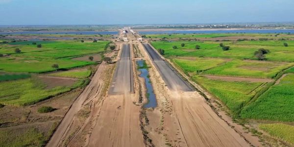 A partially constructed highway surrounded by green fields and water bodies.