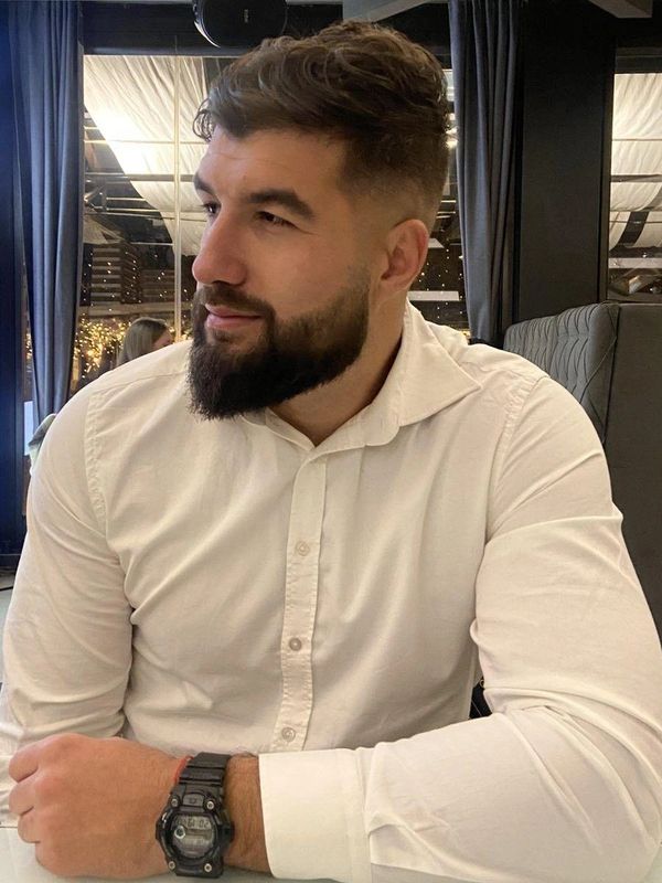 Man with beard in white shirt sitting at a table inside a restaurant.