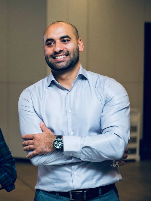 Smiling man in a light blue shirt with arms crossed, wearing a watch.