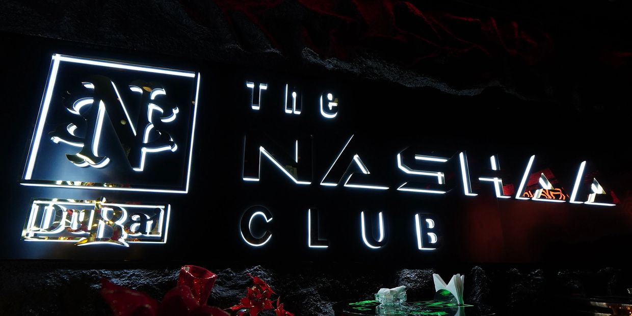 Illuminated sign for The Nashaa Club in Dubai with festive decor.