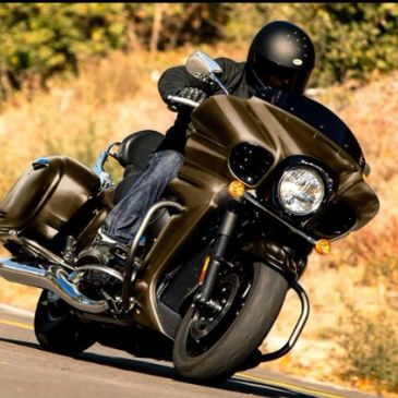 A motorcyclist in black gear riding a brown touring motorcycle on a winding road.