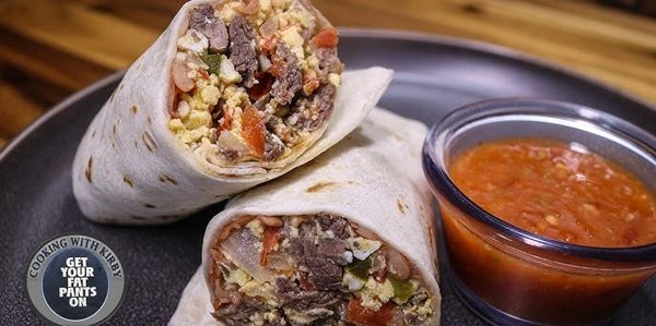 Breakfast burrito halves with steak, eggs, and salsa on a plate.