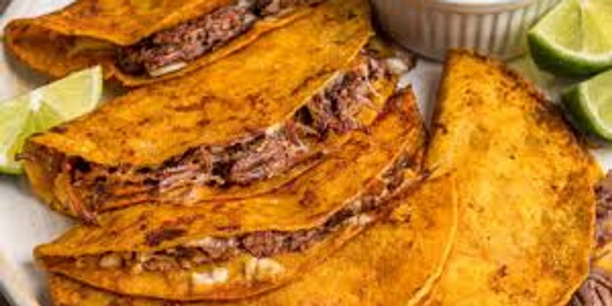 Plate of crispy beef tacos with lime wedges and dipping sauce.