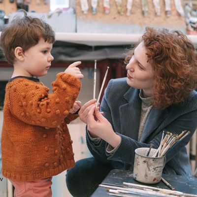 Woman holding up two paint brushes in front of child, who is pointing at one of them