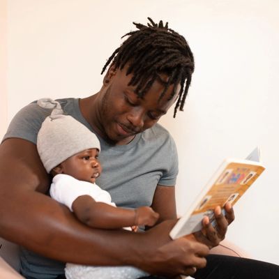 Man reading a book to a baby sitting in his lap