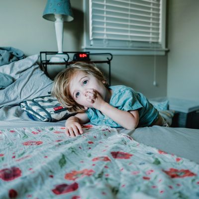 Child leaning on bed whilst sucking their thumb