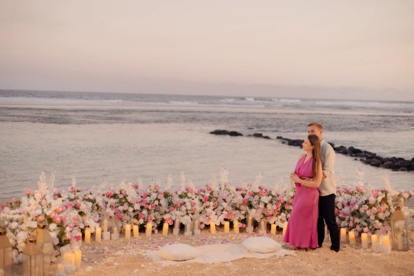 Couple embracing by the beach surrounded by flowers and candles.