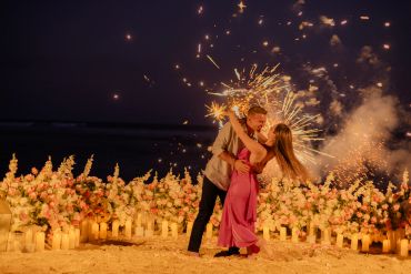 Couple dancing with sparklers on a flower-decorated beach at night.