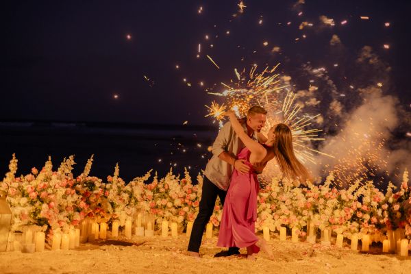 Couple dancing with sparklers on a flower-decorated beach at night.