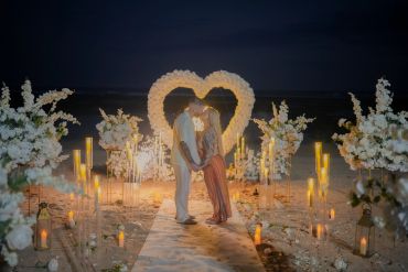 Couple kissing surrounded by heart-shaped flowers and candles at night.