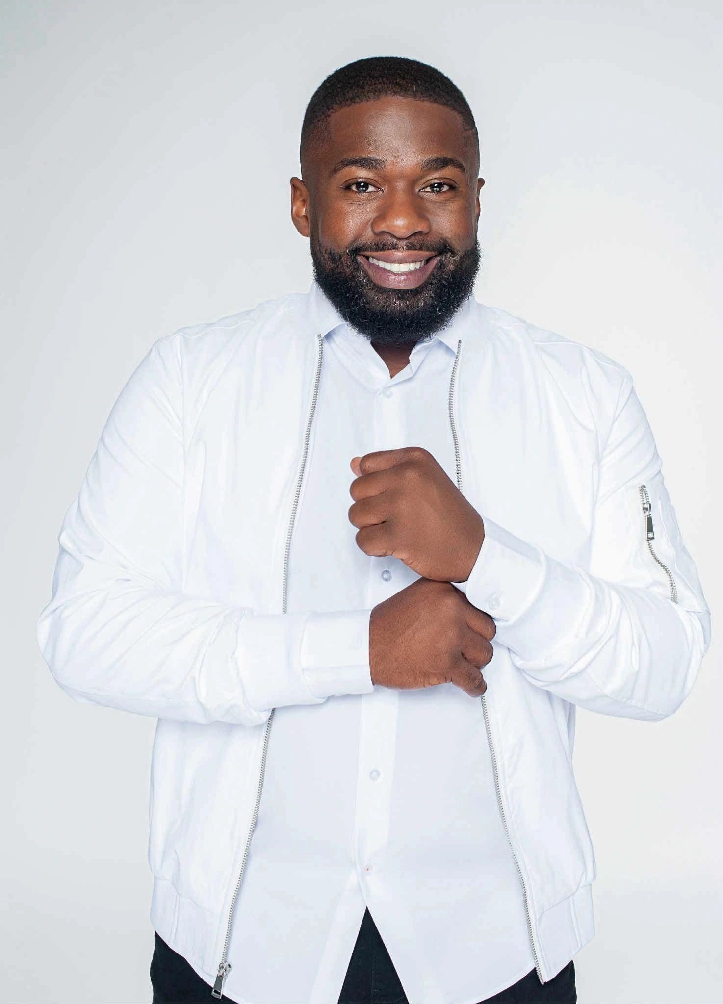 Smiling man wearing a white jacket and shirt against a plain background.