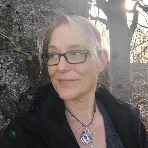 Frau mit Brille lehnt an Baum im Sonnenlicht.