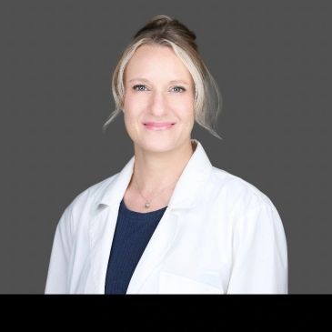 Smiling woman in white lab coat against gray background.