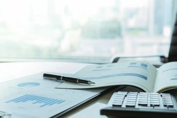 Pen on business report with calculator on desk.