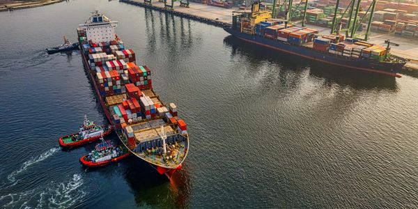 Busy container ships dock at a bustling port with cranes and colorful cargo containers.