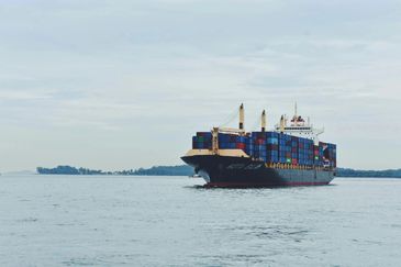 A large container ship loaded with colorful shipping containers sails on calm waters.