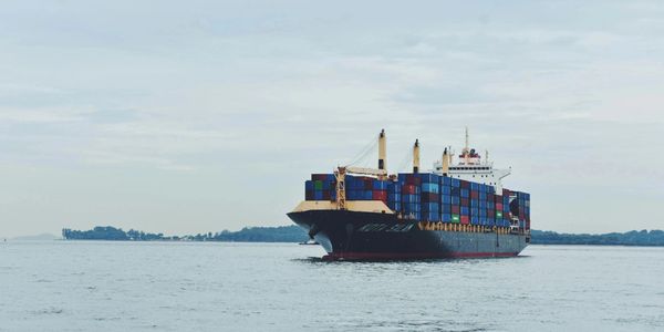 A large container ship loaded with colorful shipping containers sails on calm waters.