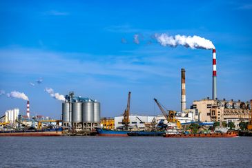 Industrial area with smokestacks emitting white smoke under a clear blue sky.