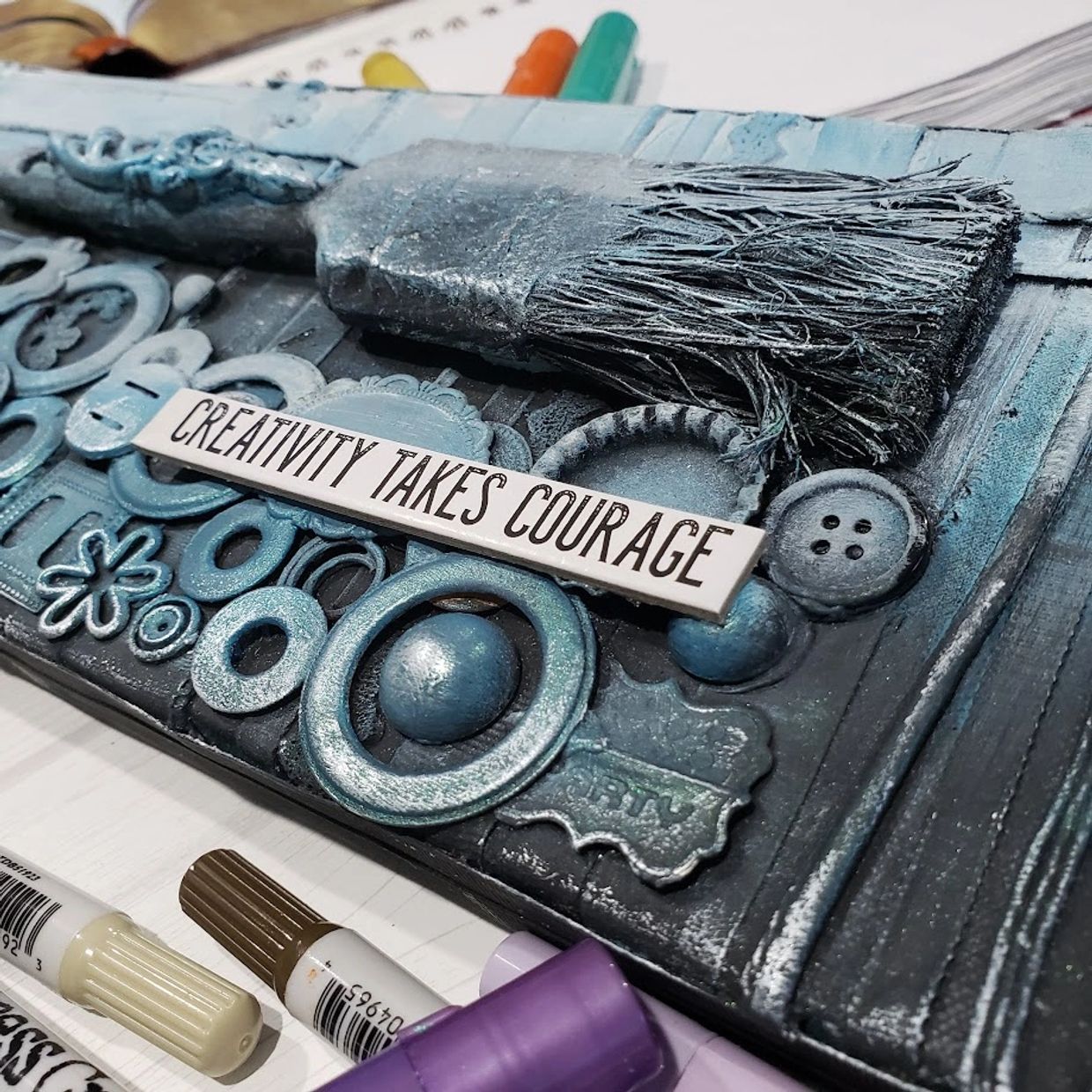 A textured art piece with a paintbrush and the phrase 'Creativity Takes Courage.'