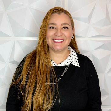 Smiling woman with long hair in black sweater and polka dot collar.