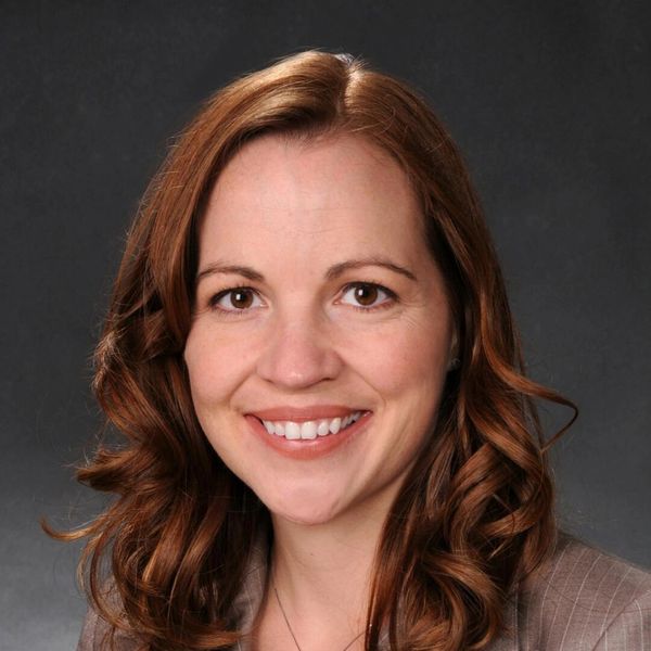 Smiling woman with wavy brown hair in professional attire.