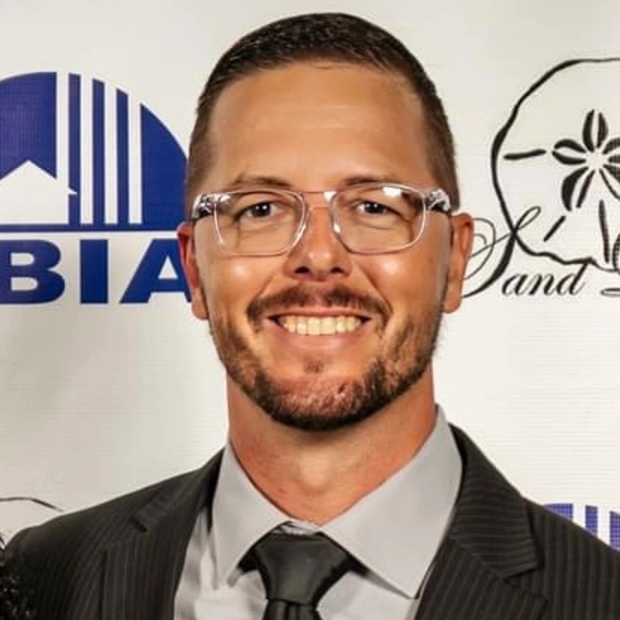 Smiling man in suit and glasses at an event.