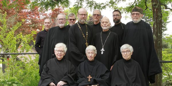 Group of monks and nuns outside under green trees dressed in black robes
