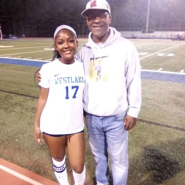 A young female athlete in Westlake uniform poses with an older man on a sports field.
