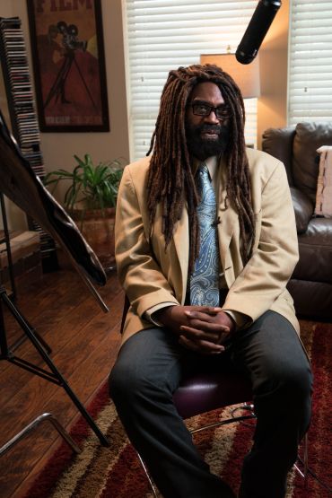Man with dreadlocks sitting for an interview in a cozy room.