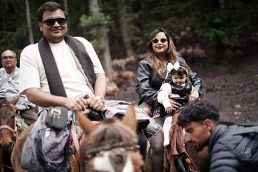 Family enjoying a horseback ride in a forested area.
