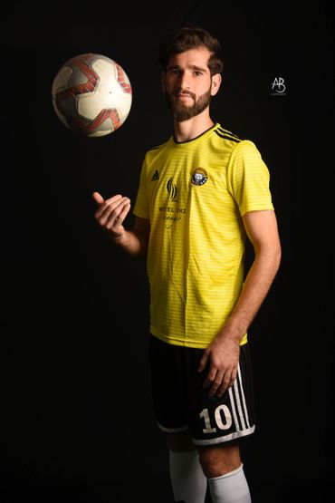 Soccer player in yellow jersey tossing a ball against a black background.