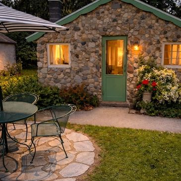 Cozy stone cottage with green door and outdoor seating at dusk.