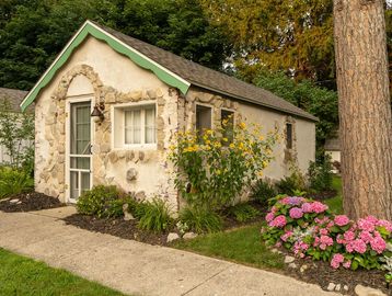 Small rustic stone garden shed surrounded by flowers and greenery.