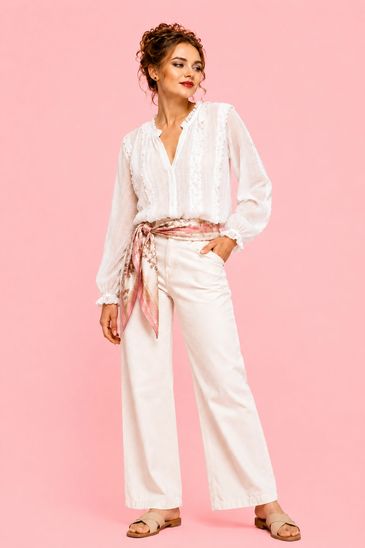 Woman in white blouse and wide-leg pants with a pink scarf belt.