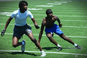 Two young men sprinting and training on a football field on a sunny day.