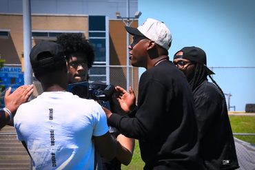 Group of young men filming outdoors with a camera on a sunny day.