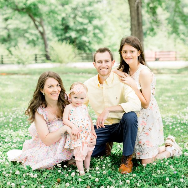 A happy family of four posing outdoors on a sunny day.