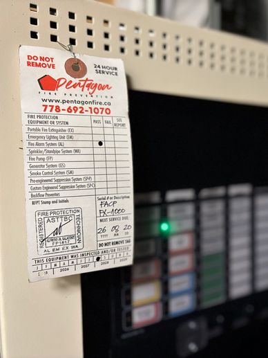 Fire protection system inspection tag on a control panel with blurred background.